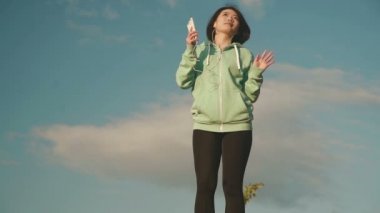 Mutlu şirin Asyalı kız gülümser gökyüzü arka plan ve müzik dinlemek