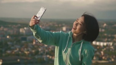 Selfie çekici ve Komik suratlar telefonunu kullanarak Park'ta açık yapma güzel Japon bayanı. Bulanık şehir arka plan