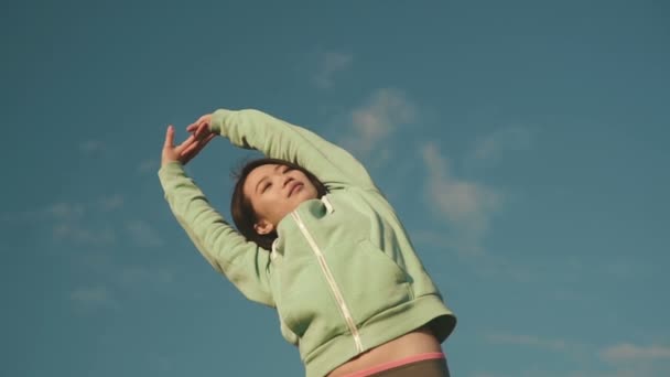 Jovem mulher asiática alongamento músculos durante o treino ao ar livre. Sorrindo feliz mestiço asiático chinês. Modelo de fitness esporte no fundo do céu — Vídeo de Stock