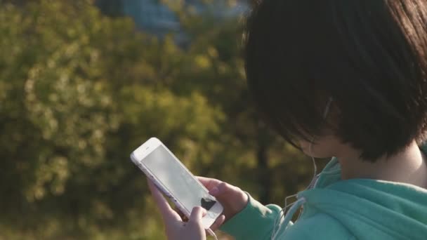 Menina de raça mista bonita com texto de cabelo curto no telefone ao ar livre no fundo do parque verde, visão traseira — Vídeo de Stock