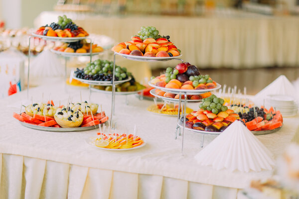 Dishes with fruits on catering banquet table decorated by white napkins
