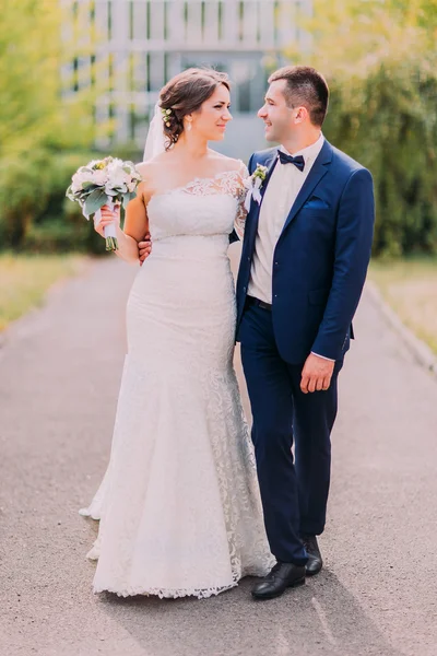 Newly married couple posing in sunny park at alley. Beautyful bride holding her bridal bouquet — Stock Photo, Image