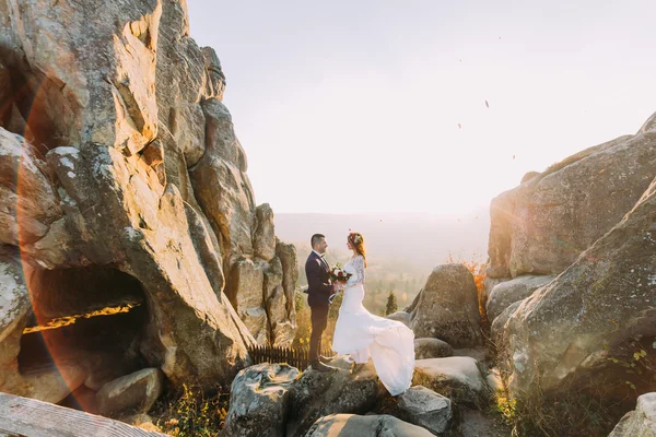 Portrait de beau couple de jeunes mariés dans les lumières du coucher du soleil sur majestueux paysage de montagne avec de gros rochers comme arrière-plan — Photo