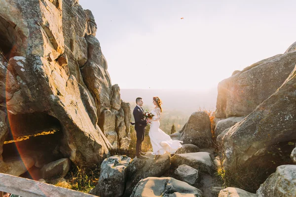 Portret romantyczny newlywed para w zachód słońca światła na majestatyczne góry krajobraz z dużymi kamieniami jak backround — Zdjęcie stockowe