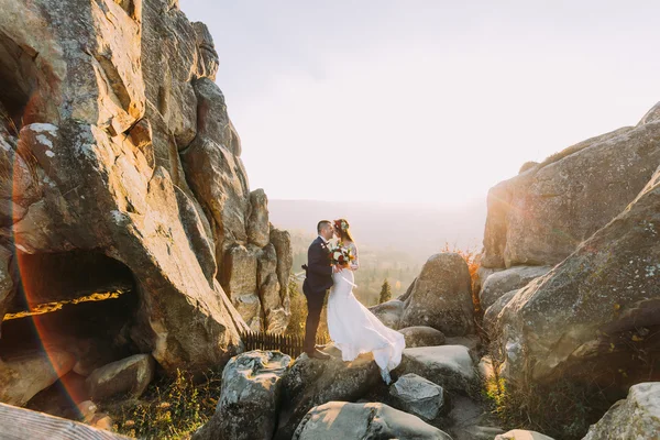 Romantikus newlywed pár a sárga naplemente fényei, a fenséges hegyi tájjal nagy sziklák, mint a hátsó szobai portréja — Stock Fotó