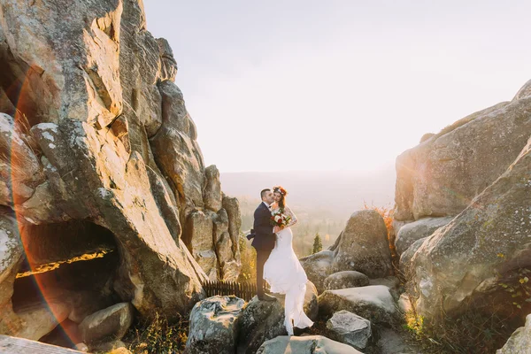 Portret van romantische jonggehuwde paar houden elkaar in zonsondergang lampjes op de majestueuze berglandschap met grote rotsen als backround — Stockfoto
