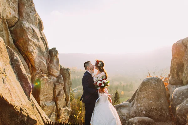 Portret van romantische jonggehuwde paar gonna kus in zonsondergang licht op de majestueuze berglandschap met grote rotsen als backround — Stockfoto