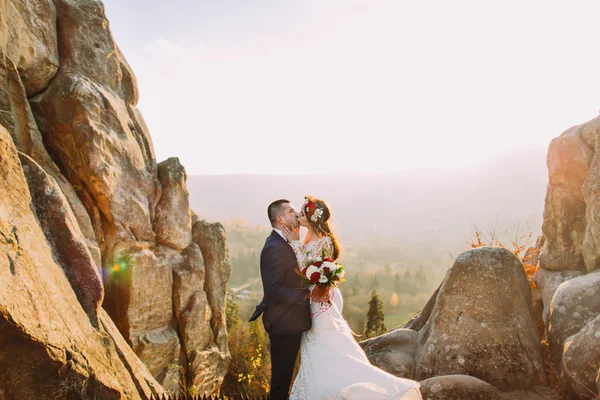 Портрет молодоженов, целующихся в лучах заката на удивительном горном ландшафте с большими скалами на заднем плане — стоковое фото