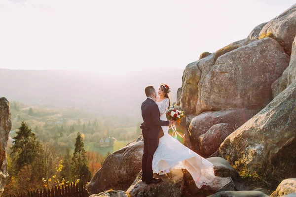 Retrato de pareja romántica recién casada besándose en las luces del atardecer en majestuoso paisaje de montaña con grandes rocas como fondo — Foto de Stock