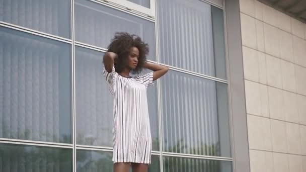 Seksikäs afrikkalainen amerikkalainen liikenainen lyhyessä viettelevä mekko poseeraa lasitoimiston seinällä. Kameran liike — kuvapankkivideo