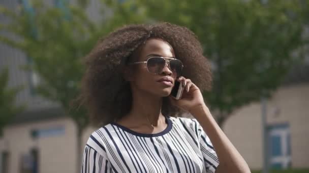 Уверенная молодая африканская деловая женщина в солнечных очках разговаривает по телефону. Городской пейзаж — стоковое видео