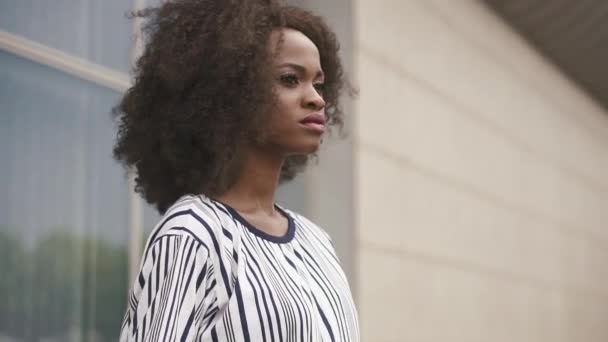 Nahaufnahme des Gesichts einer sexy afrikanisch-amerikanischen Geschäftsfrau in einem kurzen verführerischen Kleid, die an der gläsernen Bürowand posiert. — Stockvideo
