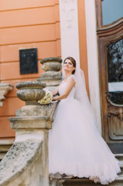Uzun kuyruk merdiven korkuluk çubuğu yakınındaki romantik vintage bina poz ile zarif beyaz elbiseli güzel gelin