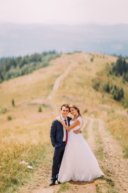 Forest Hills arka plan olarak altın güneşli araziyi izinde yürüyen güzel genç Düğün çifti