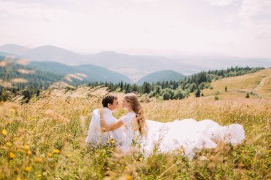 Romantik Çift sarı güneşli alan arka plan olarak orman hills ile çim oturuyor. Arkadan Görünüm