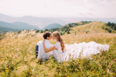 Romantik Çift sarı güneşli alan arka plan olarak uzak Orman Hills çimlere oturup