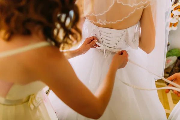 Bridemaiden ajuda a vestir noiva seu vestido de noiva branco — Fotografia de Stock