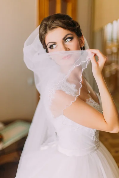 Красива наречена в білій весільній сукні приховує своє обличчя за завісою. Жіночий портрет у весільній сукні для весілля — стокове фото