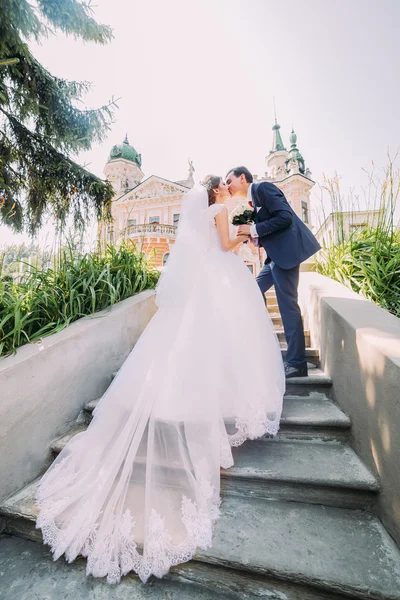 Porträt eines eleganten jungen Hochzeitspaares, das sich auf einer Treppe im Park küsst. romantischer antiker Palast im Hintergrund — Stockfoto