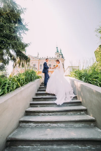 Casal de casamento jovem bonito em escadas no parque. Palácio antigo romântico no fundo — Fotografia de Stock