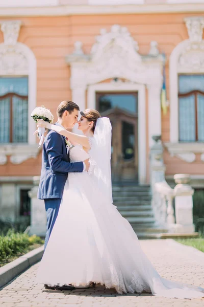 Pareja romántica recién casada novia encantadora y elegante novio abrazándose entre sí en frente de la entrada del edificio antiguo —  Fotos de Stock