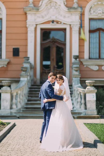 Romantic newly married couple charming bride and stylish groom posing in front of antique building entrance — Stock Photo, Image