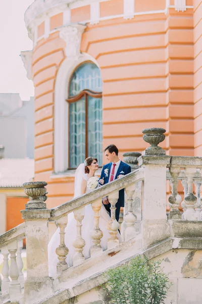 Belos jovens recém-casados nas escadas do parque. Edifício vintage velho no fundo — Fotografia de Stock