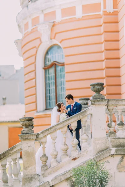 Bonito par de casamento jovem posando nas escadas no parque. Edifício vintage romântico no fundo — Fotografia de Stock