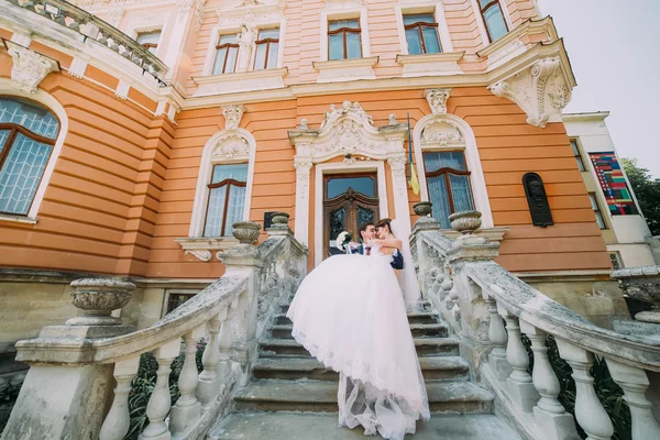 Casal amado nas escadas do palácio antigo romântico. noivo segurando bela noiva em suas mãos — Fotografia de Stock