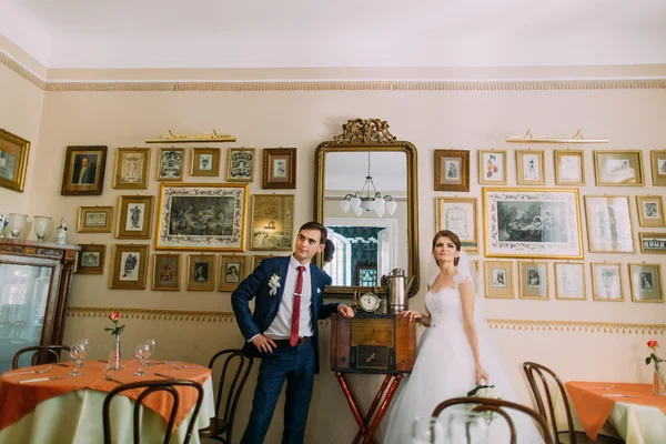 Жених и невеста позируют в ретро-кафе с красивым винтажным интерьером после свадьбы — стоковое фото