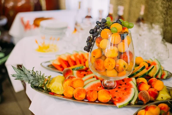 Owoce, catering tabeli z soczyste ananasy, winogrona, arbuz i brzoskwinie w szklanym wazonie — Zdjęcie stockowe