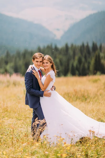 Pareja de boda de moda y feliz abrazándose en el campo soleado con fondo de bosque —  Fotos de Stock
