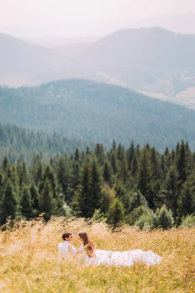 Coppia romantica seduta in erba a giallo campo soleggiato con colline forestali come sfondo — Foto Stock