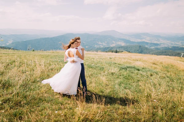 Casal romântico jovem posando no campo ensolarado ventoso com colinas distantes da floresta como fundo — Fotografia de Stock