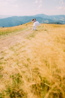 Arka plan olarak uzak orman tepeleri ile rüzgarlı altın güneşli alan üzerinde poz genç romantik düğün çift
