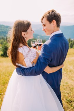 Neşeli yeni evliler dışarıda şarap içiyorlar, evliliklerini kutluyorlar. Doğa arka planı ile yakın çekim