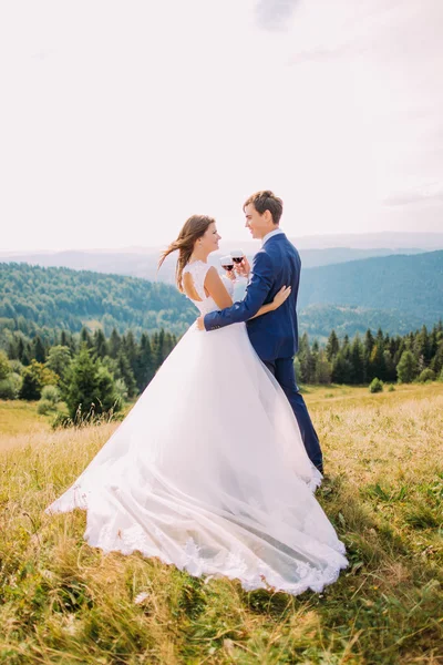 Recém-casados alegres bebendo vinho ao ar livre, celebrando seu casamento. Natureza fundo — Fotografia de Stock