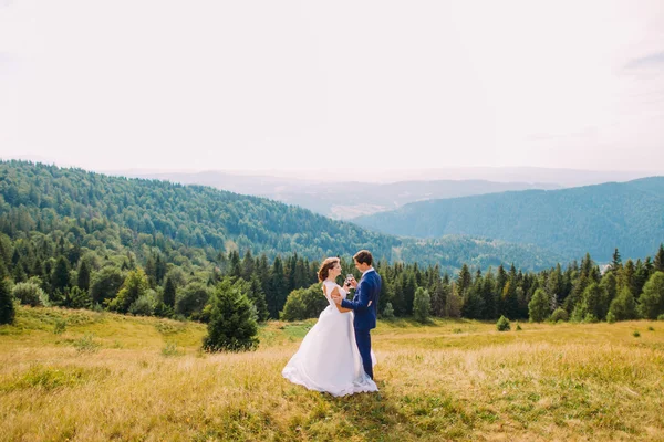 Casal alegre apenas casado bebendo vinho ao ar livre, celebrando seu casamento. Fores colinas fundo — Fotografia de Stock