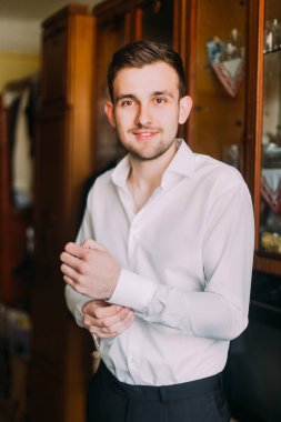 Beyaz gömlekli genç adam, kol düğmelerini içeri sokuyor.