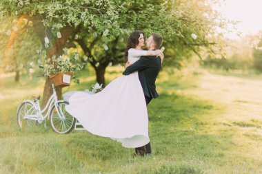 Mutlu sadece yeşil güneşli parkta çim üzerinde dans evli. Arka planda dekore edilmiş ağacın yanında bisiklet