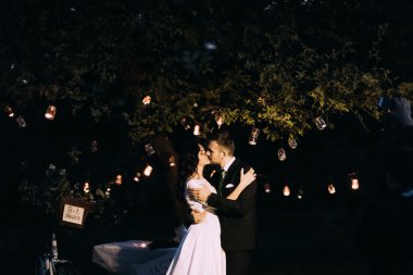 Güzel gelin ve damat akşam Park ağaç altında öpüşme çok fener ile dekore edilmiş