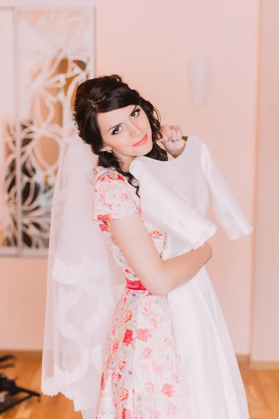 Menina bonita segurando vestido de casamento de seda no camarim, preparando-se para vesti-lo para seu casamento — Fotografia de Stock