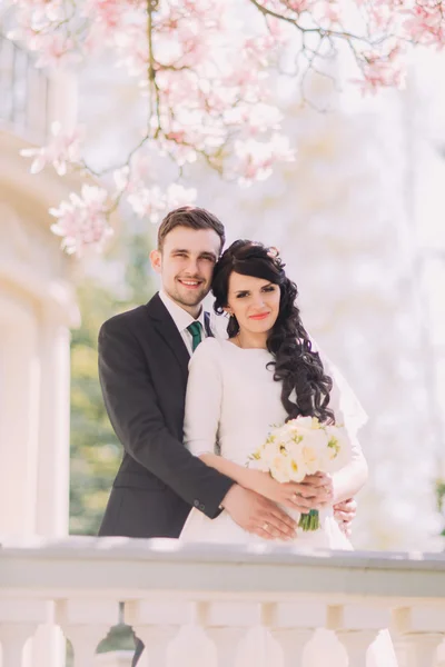 Portret van gelukkige jonggehuwden op vintage balkon onder bloeiende magnolia boom — Stockfoto