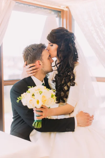 A noiva amorosa beija a testa do novo marido, sentada de joelhos. Janela no fundo — Fotografia de Stock