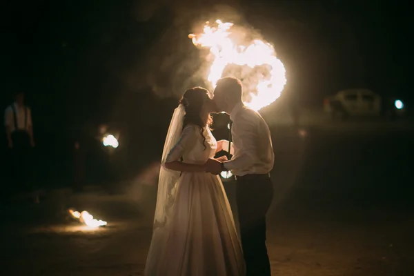 Romântico recém-casados beijando à noite na frente do coração flamejante — Fotografia de Stock