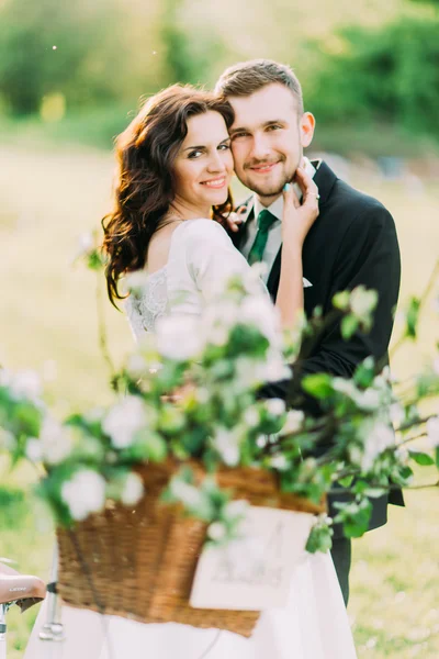 Retrato de feliz jovem casal recém-casado no parque com decoração floral borrada em primeiro plano — Fotografia de Stock