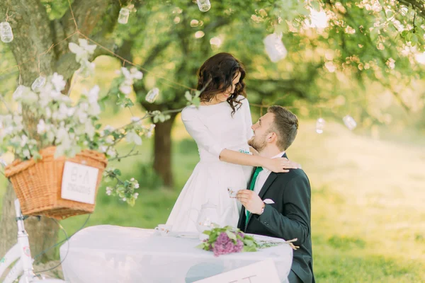 Picknick romântico no parque. noiva brincalhão abraçando seu lindo novo marido enquanto ele bebe chá — Fotografia de Stock