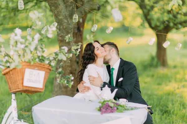 Romantisches Picknick im Park. Paar umarmt sich beim Teetrinken unter Baum, geschmückt mit kleinen Glaslaternen — Stockfoto