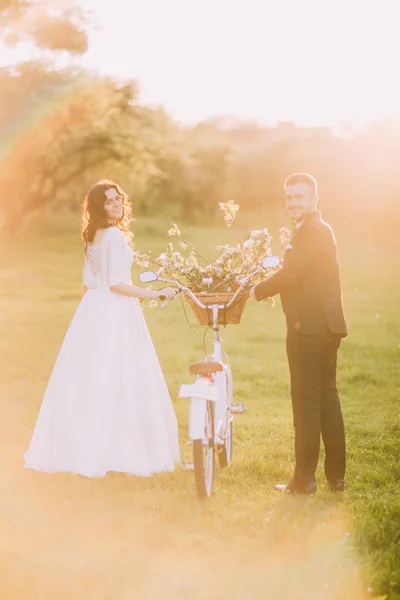 Pareja romántica paseando por el soleado parque con bicicleta decorada entre ellos. Bengalas cálidas — Foto de Stock