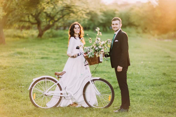 Pareja romántica posando en un parque soleado con bicicleta decorada entre ellos. Bengalas cálidas del sol — Foto de Stock